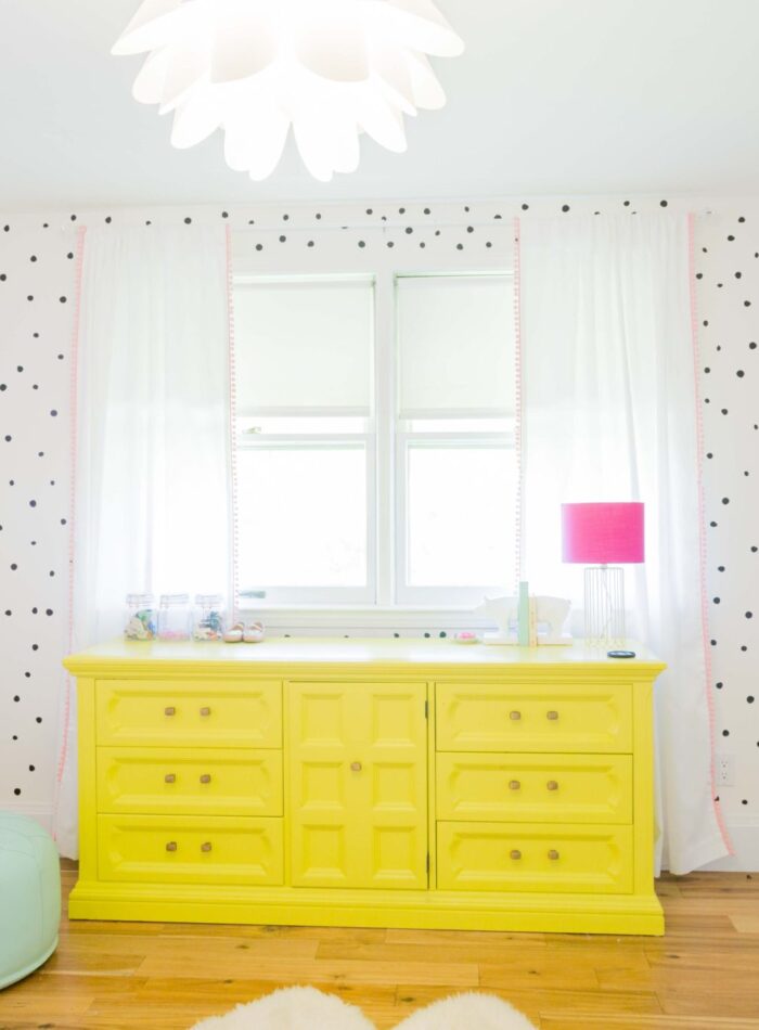 pretty and bright girls bedroom | bright nursery for baby girl | yellow dresser | the lovely wall co. decals | ikea picture ledge bookshelves | allweareblog.com